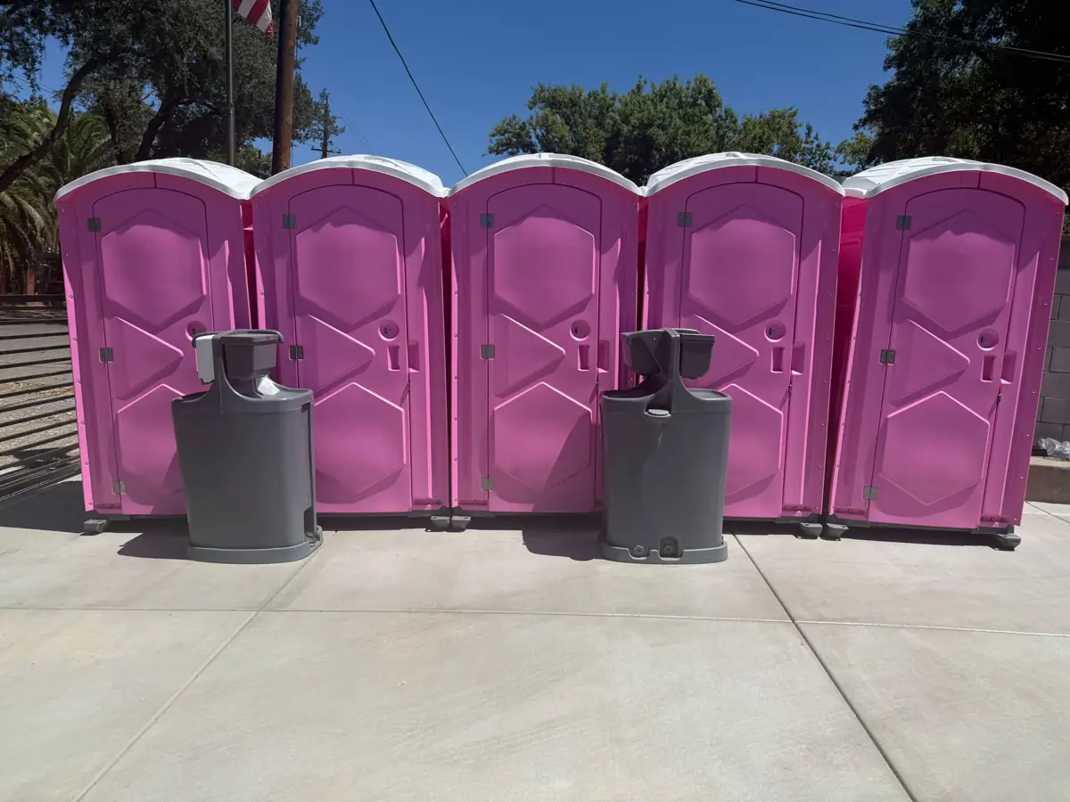 Row of pink portable toilets with two freestanding handwashing stations