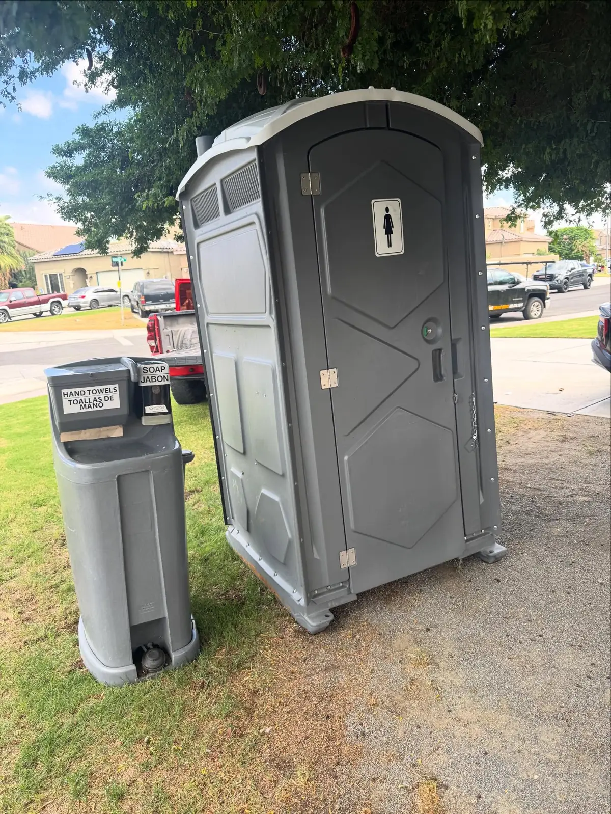 Gray portable toilet next to a handwashing station on a lawn