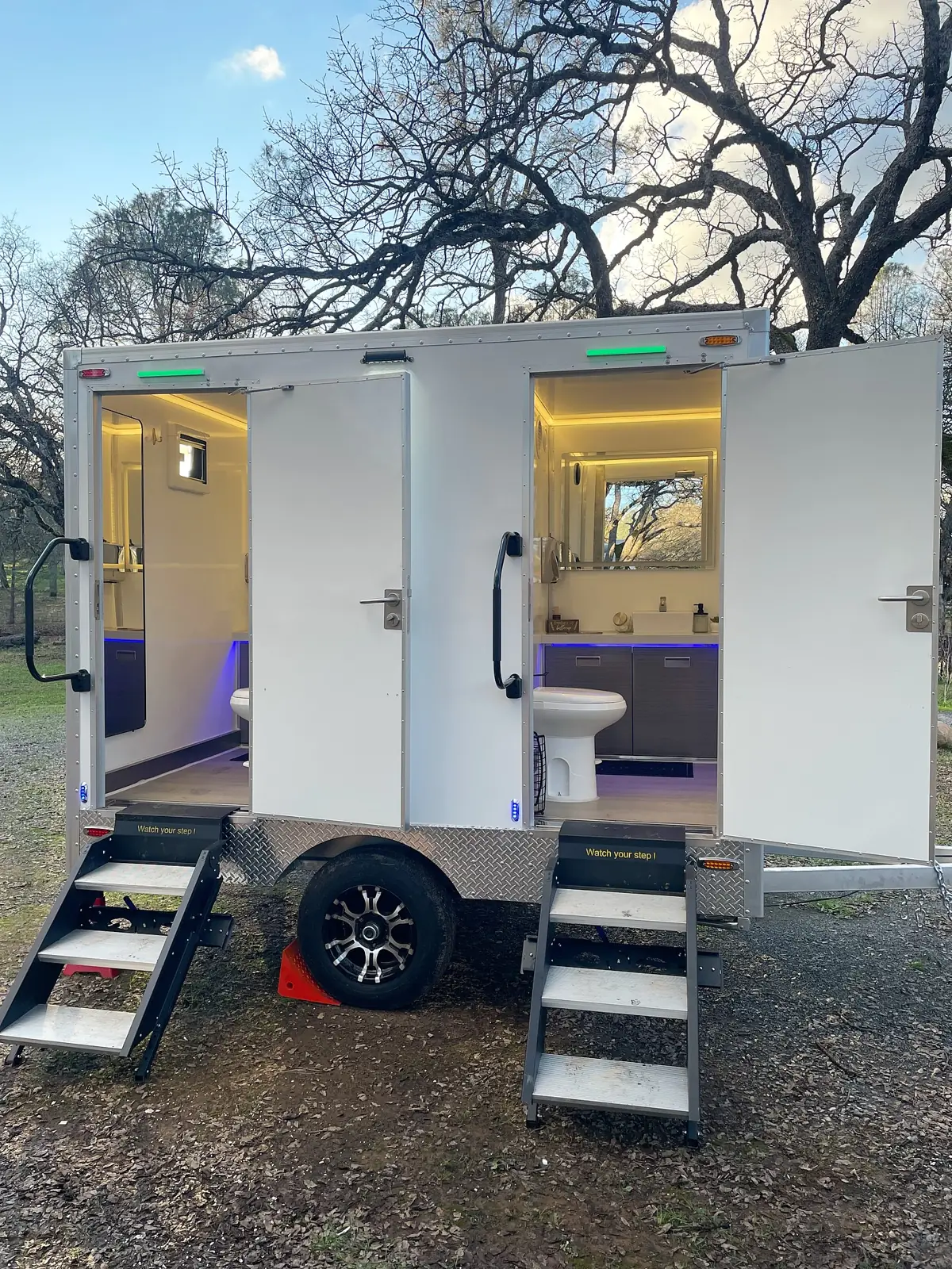 Two-stall restroom trailer with both doors open and lit interiors